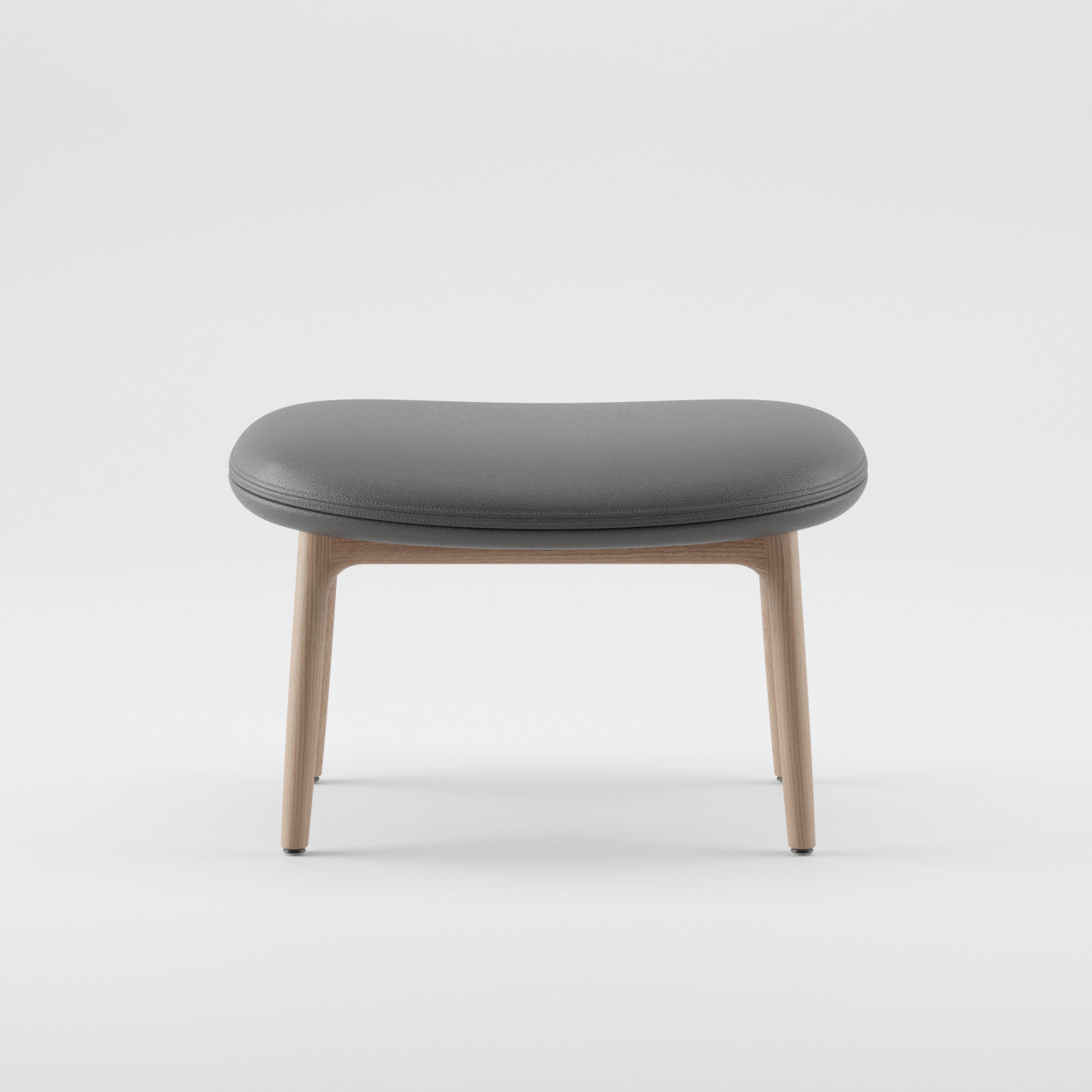 The NEVA Ottoman by Artisan showcases a minimalist design with a rounded gray cushioned seat and light wooden legs, reminiscent of modern Scandinavian lounge furniture, set against a plain white background.