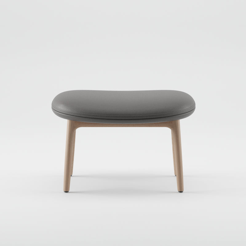 The NEVA Ottoman by Artisan showcases a minimalist design with a rounded gray cushioned seat and light wooden legs, reminiscent of modern Scandinavian lounge furniture, set against a plain white background.