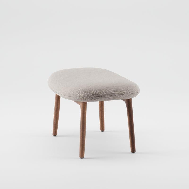 The NEVA Ottoman by Artisan features a beige upholstered cushion and wooden legs, highlighting the elegance of CNC carving, set against a plain white background.