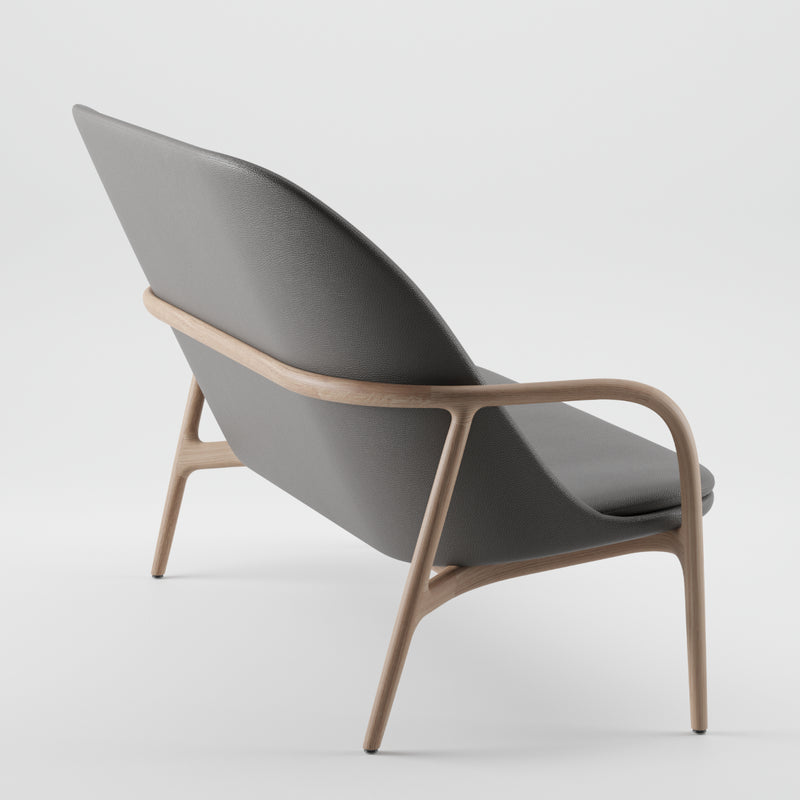 The NEVA Sofa by Artisan showcases a sleek Scandinavian design, featuring a gray upholstered seat and backrest. It has a light wooden frame with smooth, curved armrests and legs, angled to display its side and back profile against a plain white background.