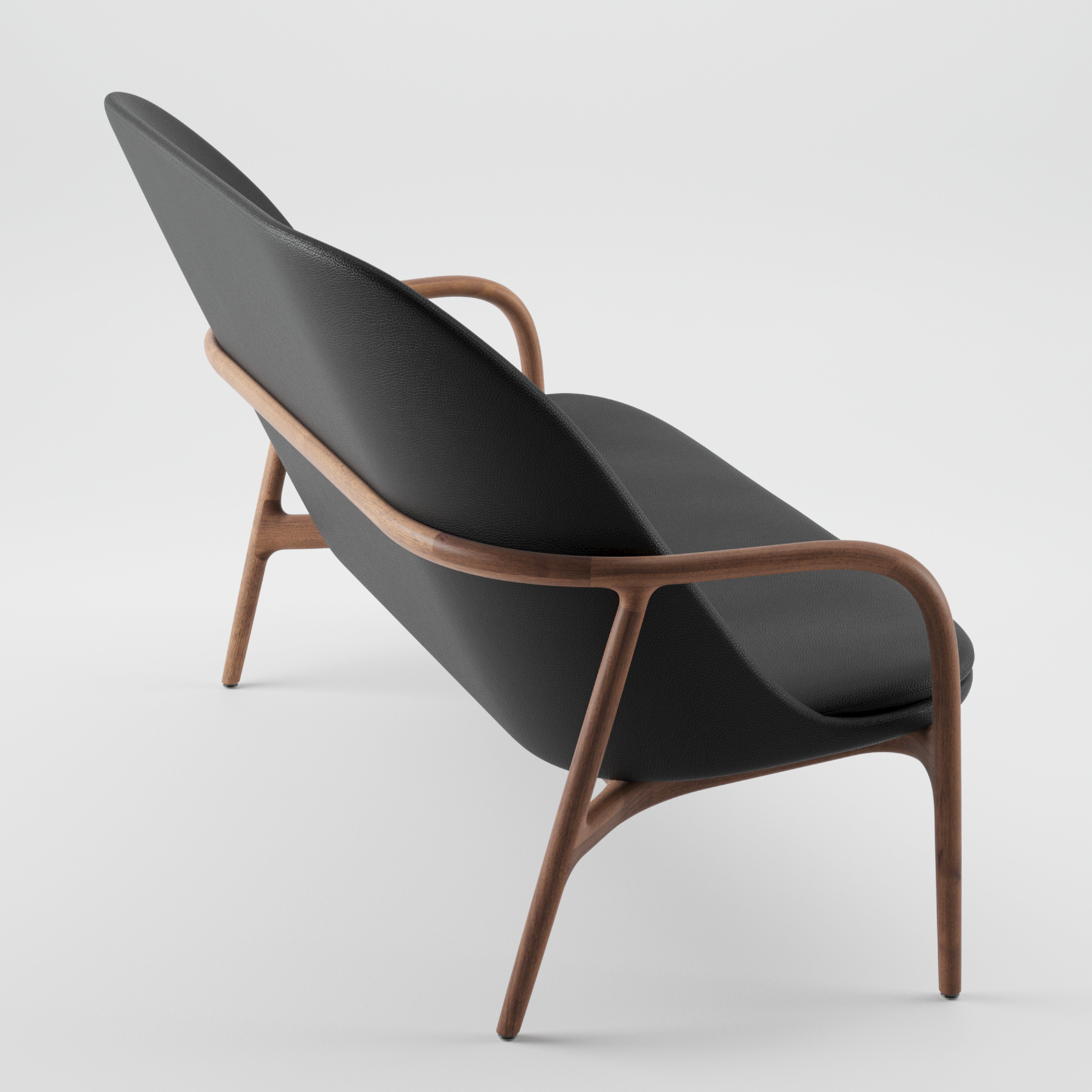 The NEVA Sofa by Artisan features a wooden frame and smooth black upholstery, showcasing sleek, curved lines inspired by Scandinavian design. Viewed from the back and side against a plain white background, it embodies a minimalist aesthetic.