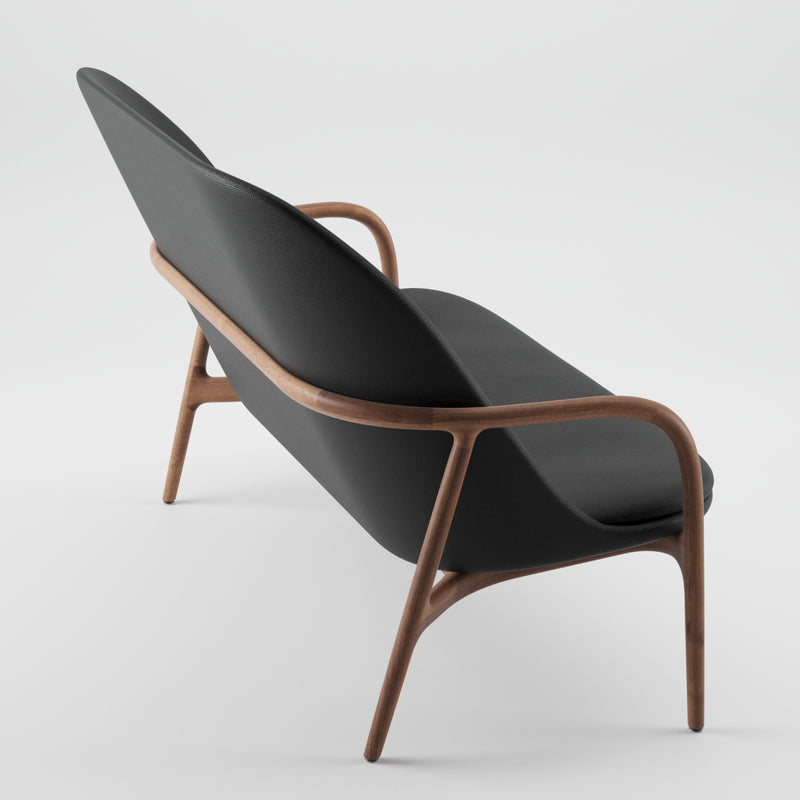 The NEVA Sofa by Artisan features a wooden frame and smooth black upholstery, showcasing sleek, curved lines inspired by Scandinavian design. Viewed from the back and side against a plain white background, it embodies a minimalist aesthetic.