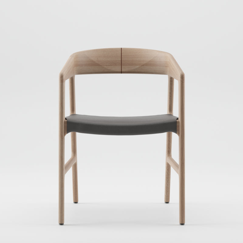 The TESA Chair by Artisan is a minimalist piece featuring a solid wood structure, light brown frame, and dark gray seat cushion. Its organic beauty is highlighted by a curved backrest and clean lines, displayed against a plain white background.