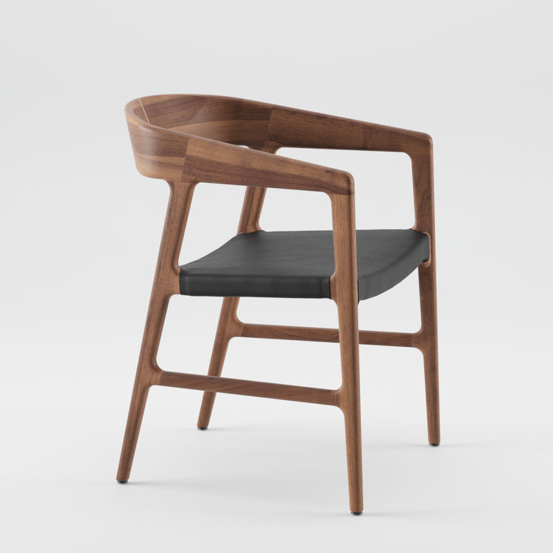 The TESA Chair by Artisan is a modern wooden chair with a sleek design made from eco-friendly materials. It features a curved backrest and armrests, complemented by a dark cushioned seat for a minimalist, elegant look against a plain white background.