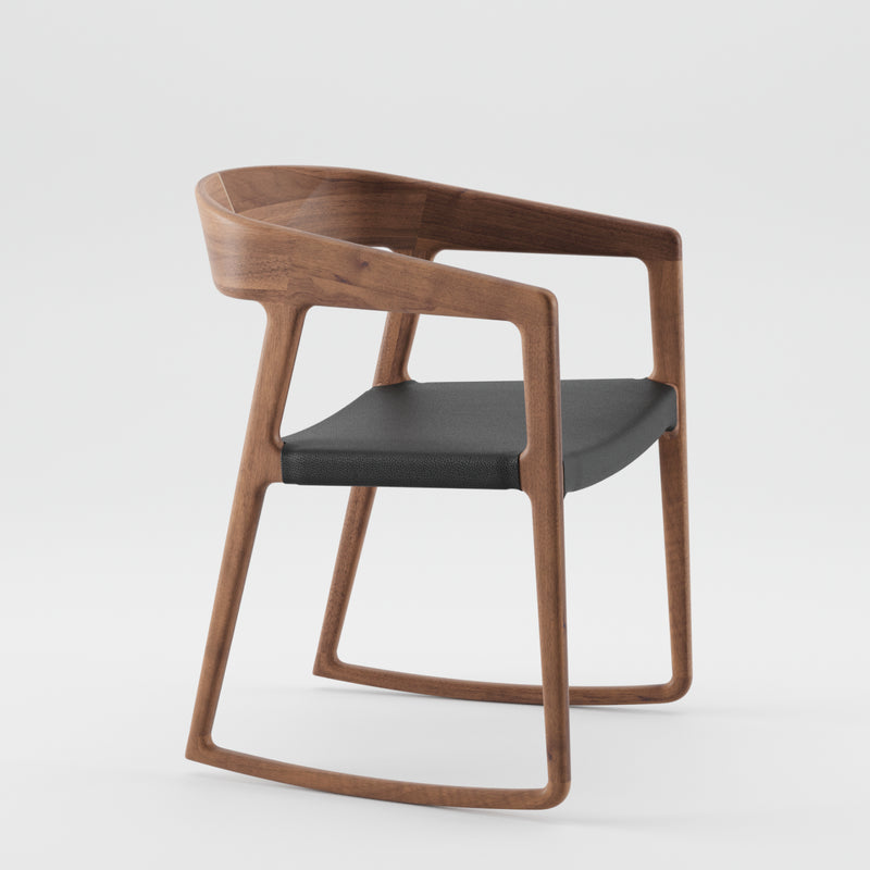 The TESA SWING CHAIR by Artisan is a modern wooden chair made from solid wood, featuring a sleek curved backrest and armrests. A black cushioned seat complements its minimalist design, finished with natural oils for eco-friendliness, set against a plain white background.
