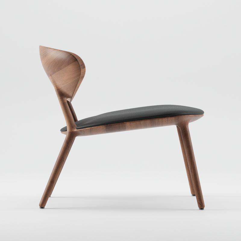 Side view of the WU Lounge Chair by Artisan, showcasing a luxurious wood texture and gently curved backrest. Sleek legs and a cushioned dark fabric seat embody minimalist elegance, crafted from eco-friendly materials, all set against a plain white background.