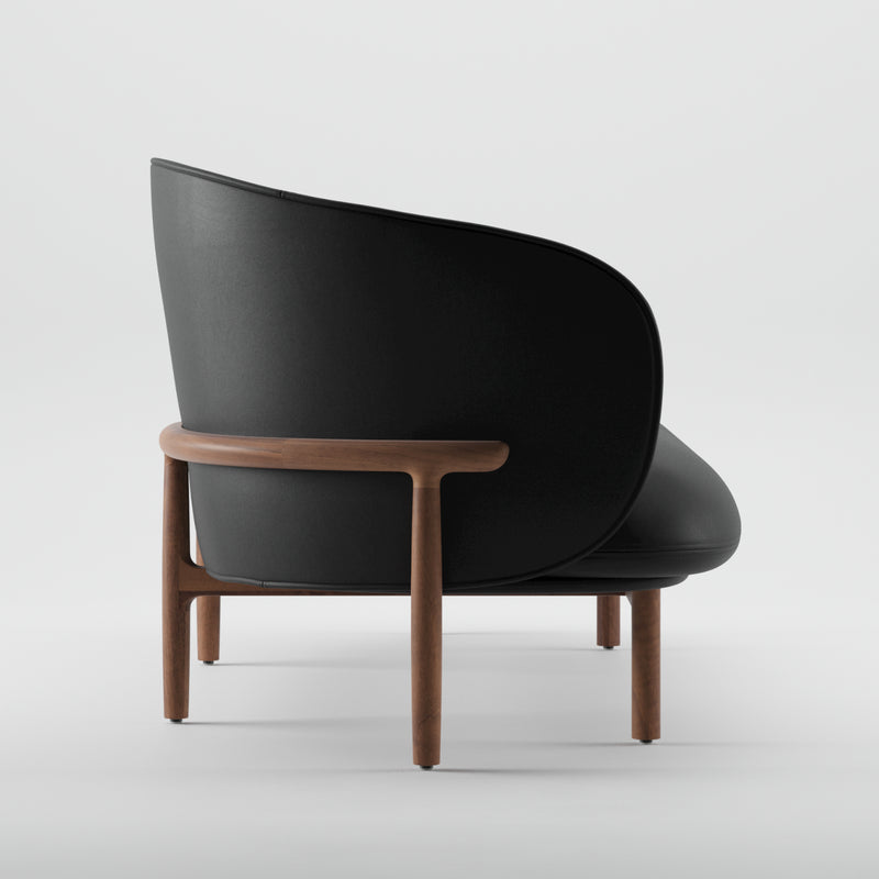 The MELA Two Seater by Artisan presents a chic black leather seat and backrest, enhanced by a wooden frame. This upholstered piece showcases a minimalist design with angled positioning to accentuate its curved back and stylish wooden legs.