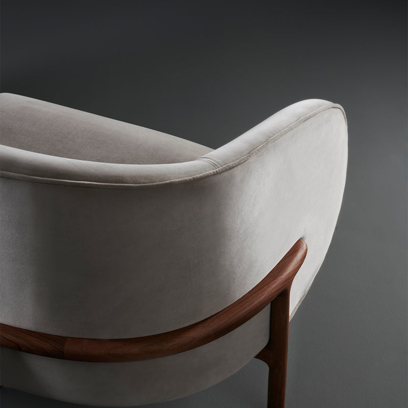 Elegant and modern, the MELA Two Seater by Artisan features a smooth, light grey upholstered backrest and seat. Its curved wooden frame has a rich brown finish, offering a striking contrast against dark settings.