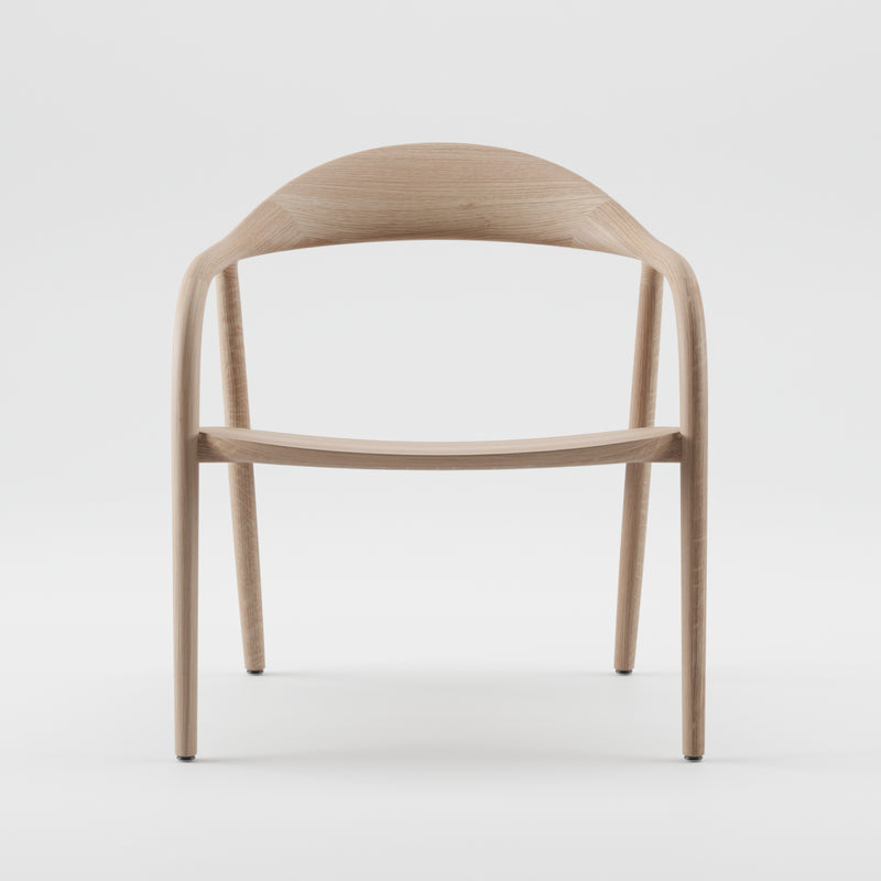 The NEVA Easy Chair by Artisan is a minimalist wooden piece with flowing curves and a light natural finish. Its ergonomic design features a rounded backrest transitioning into armrests on slender legs, crafted using precision 5-axis CNC technology for an elegant, airy appearance.