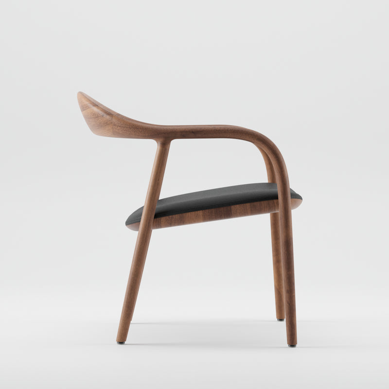 The Artisan NEVA Easy Chair boasts a modern, curved wooden frame made with 5-axis CNC technology. Its ergonomic design and comfortable cushioned black seat are elegantly displayed from the side against a white background.