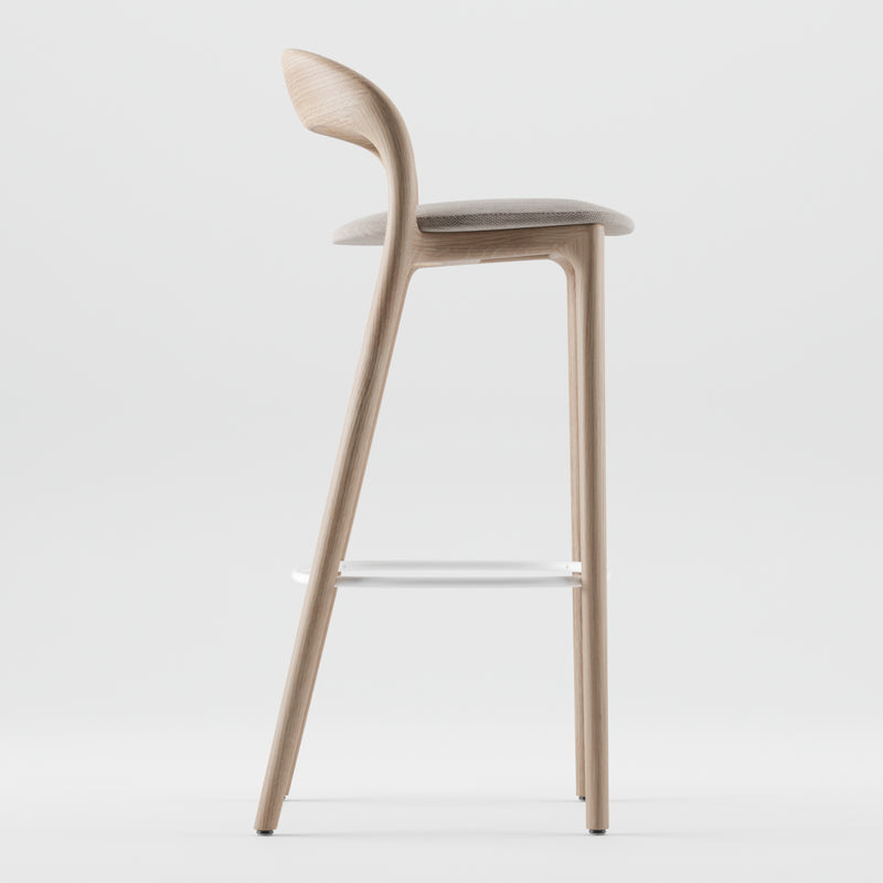 The NEVA light barstool by Artisan features a side view with a curved backrest and small cushioned seat, highlighting its artisan carpentry and minimalist design. It includes a white metal footrest, all set against a plain white background.