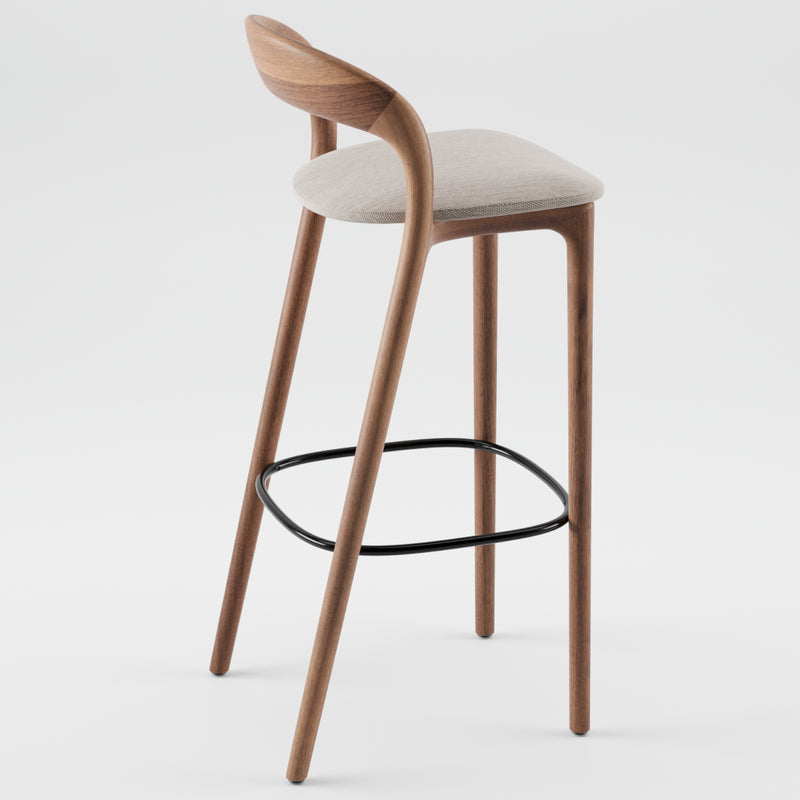 The NEVA light barstool by Artisan showcases expert carpentry with a light gray cushioned seat, a curved wooden backrest, and elegantly tapered legs. It features a modern touch with a black oval footrest seamlessly connecting the legs.