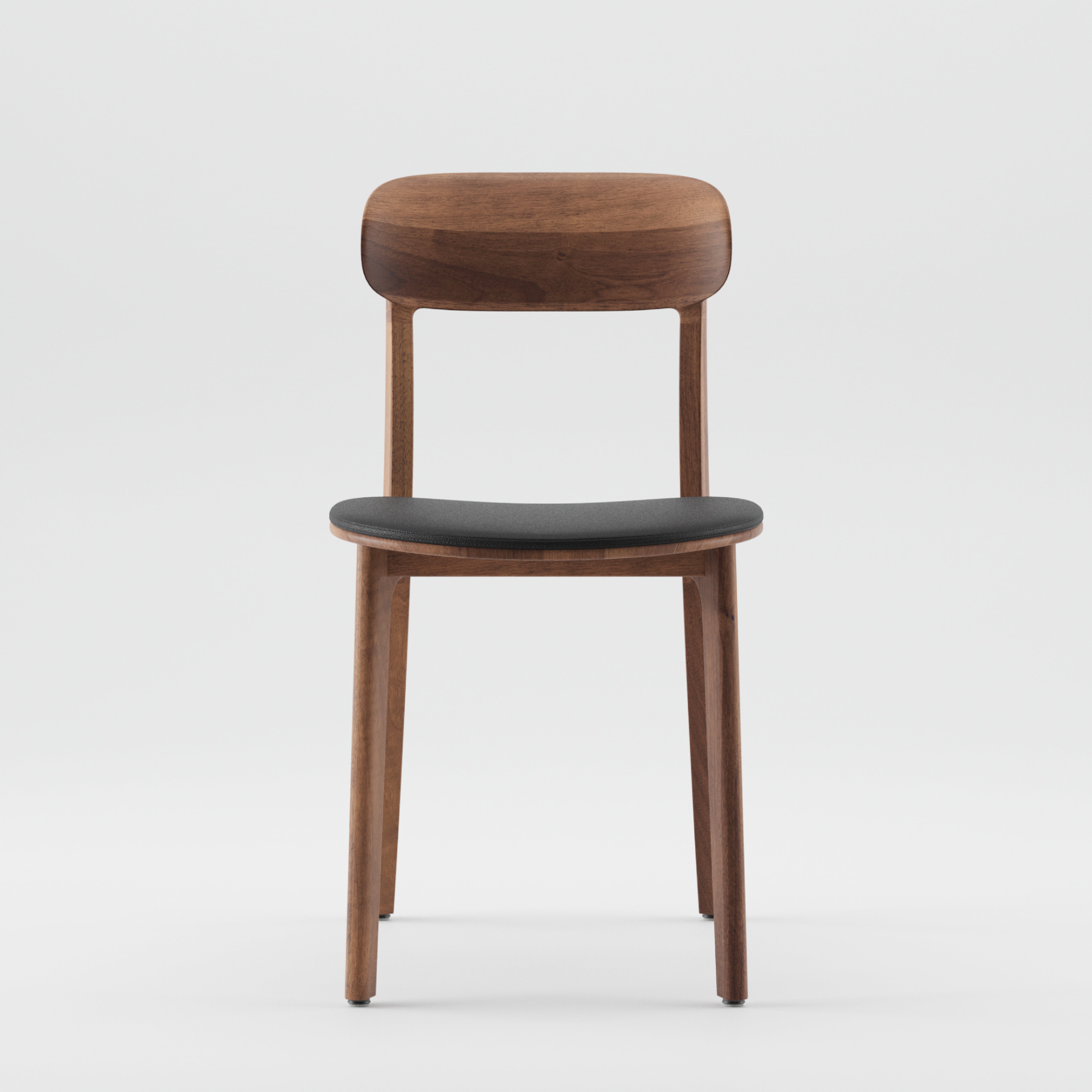 The Artisan TANKA Chair Upholstered showcases a minimalist design with a curved solid wood backrest and a black cushioned seat. Its lightweight wooden frame with four straight legs is elegantly presented against a plain white backdrop.