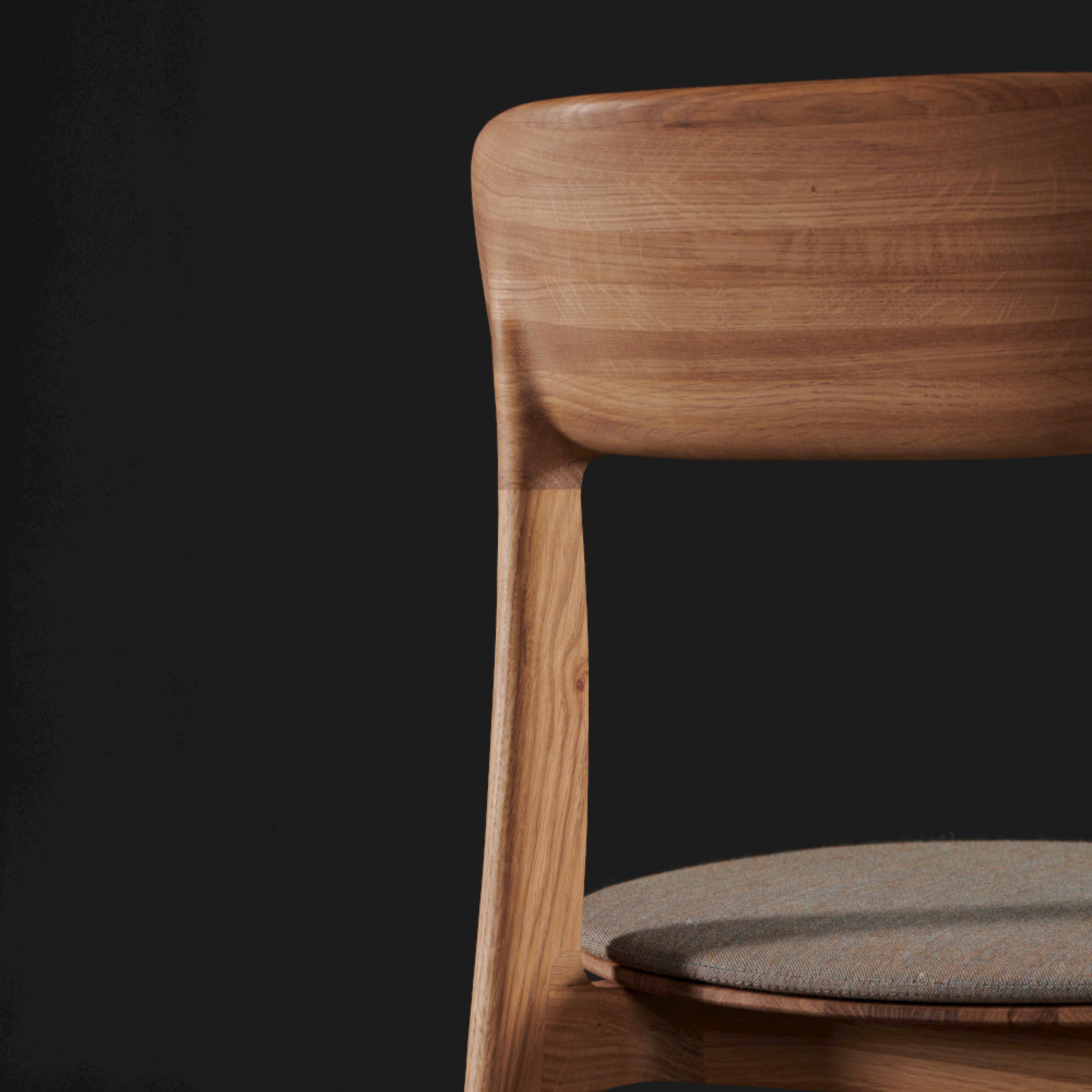A close-up of the Artisan TANKA Chair showcases its solid wood backrest with smooth curves and a cushioned seat. The natural finishes stand out against a dark background, emphasizing its exquisite wood grain.