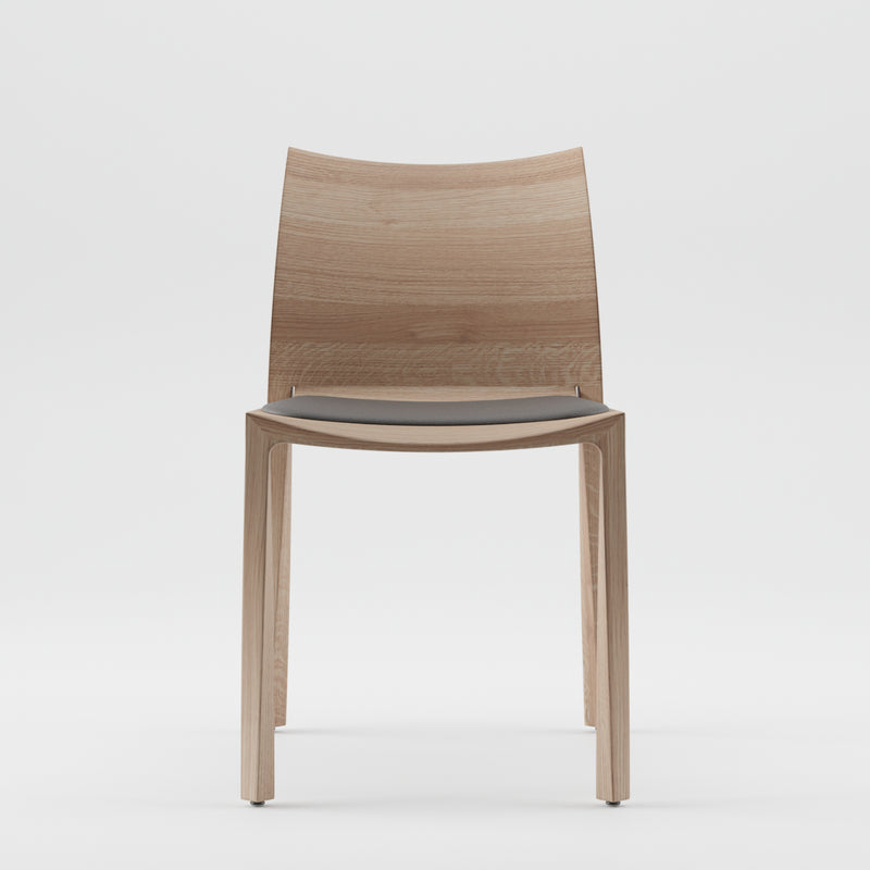 The TORSIO Chair Upholstered by Artisan features a modern minimalist design with a solid wooden frame, light brown finish with natural oils, and an environmentally-friendly build. It boasts a gently curved backrest and subtly cushioned gray seat on four straight legs.