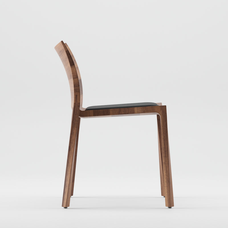 Side view of the Artisan TORSIO Chair Upholstered, featuring a solid wood build with a natural oil finish. It displays a dark cushioned seat with a sleek, minimalist design, slightly curved backrest, and straight legs against a white background.