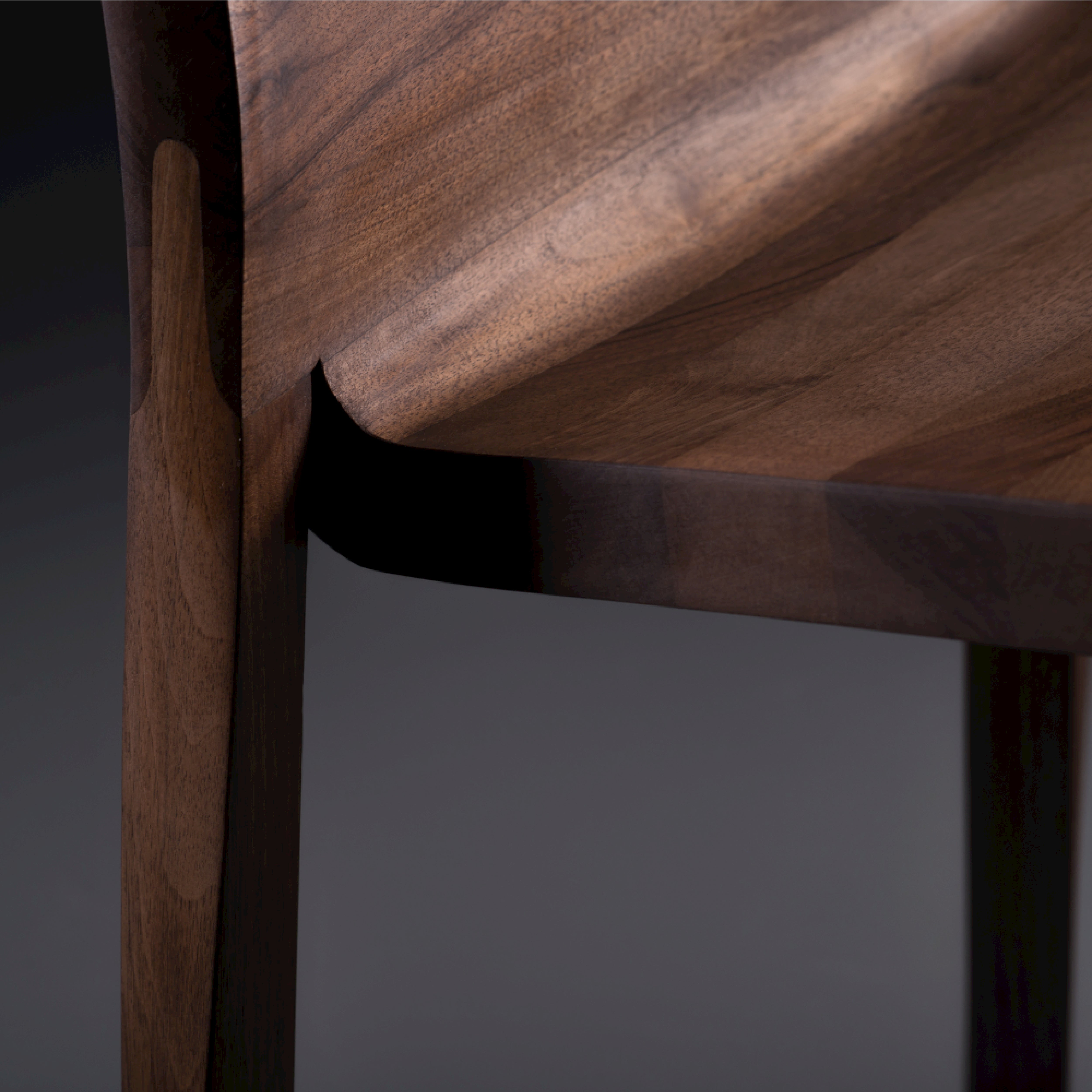 Close-up of the TORSIO Chair by Artisan, showcasing its smooth curved design and natural wood grain. The rich dark tones of solid wood contrast with soft lighting, highlighting natural oils that enhance its craftsmanship and eco-friendly elegance.