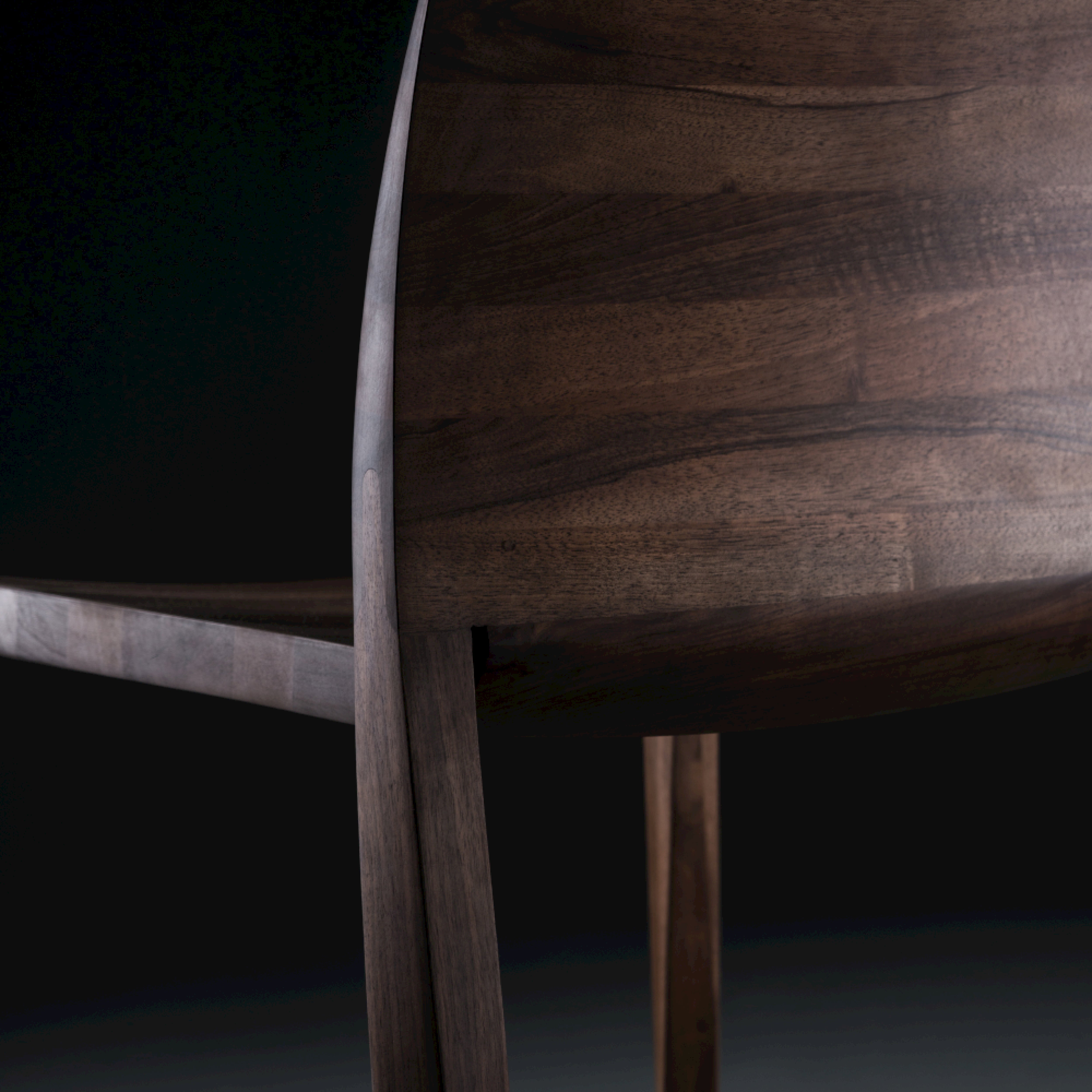 Close-up of the TORSIO Chair by Artisan, showcasing its dark solid wood structure with smooth, curved lines. The polished finish is enriched by natural oils, focusing on the backrest and part of the legs against a black background.