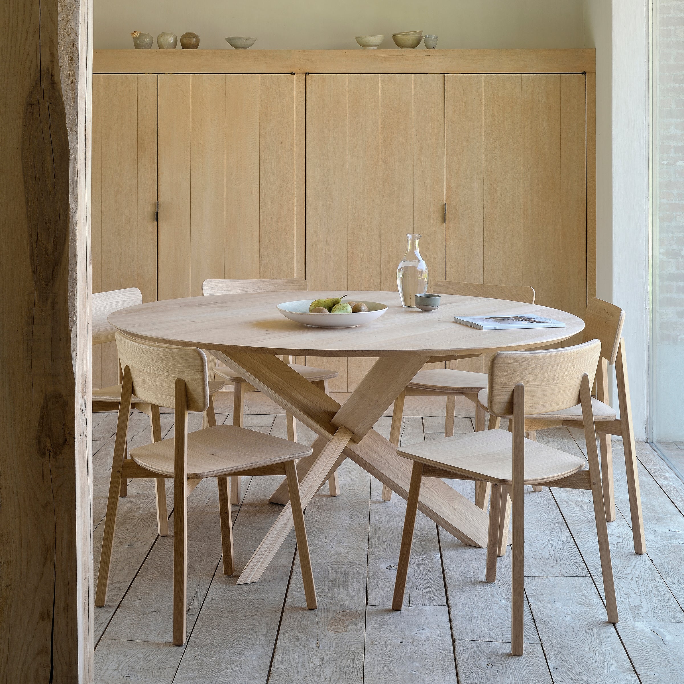 Casale Dining Chair in varnished oak with smooth lines around a round wooden dining table in a minimalist room.
