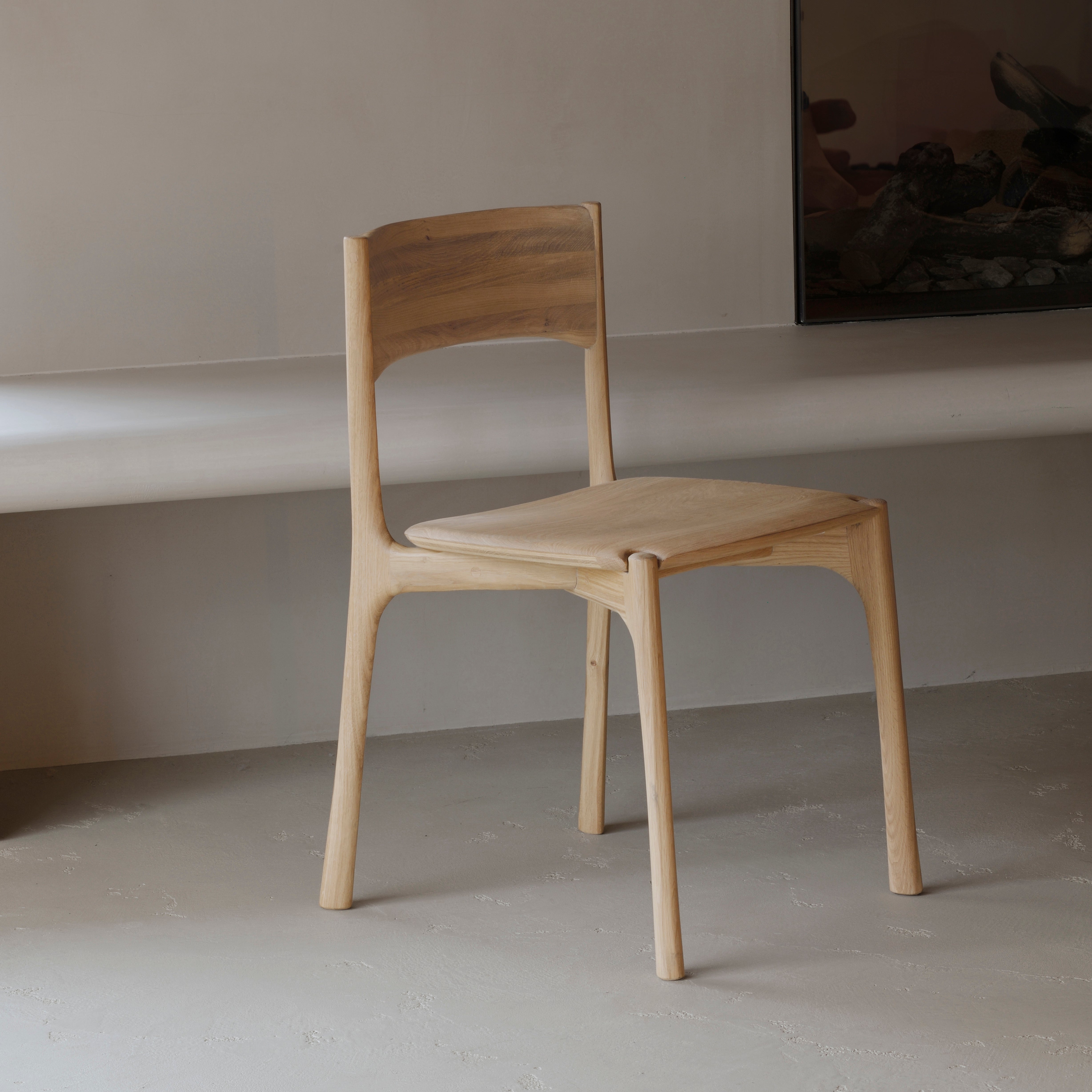 Pi Dining Chair made of oak wood with sleek, natural curves and a polished imperfect finish in a minimalist setting.