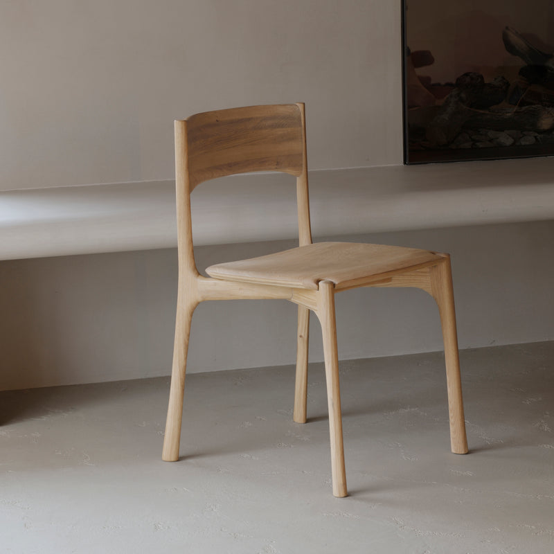 Pi Dining Chair made of oak wood with sleek, natural curves and a polished imperfect finish in a minimalist setting.