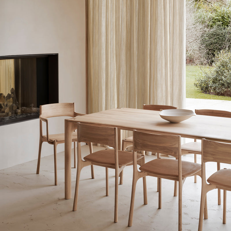 Pi Dining Chair with Armrest in oak wood around matching wooden dining table in a minimalist room.