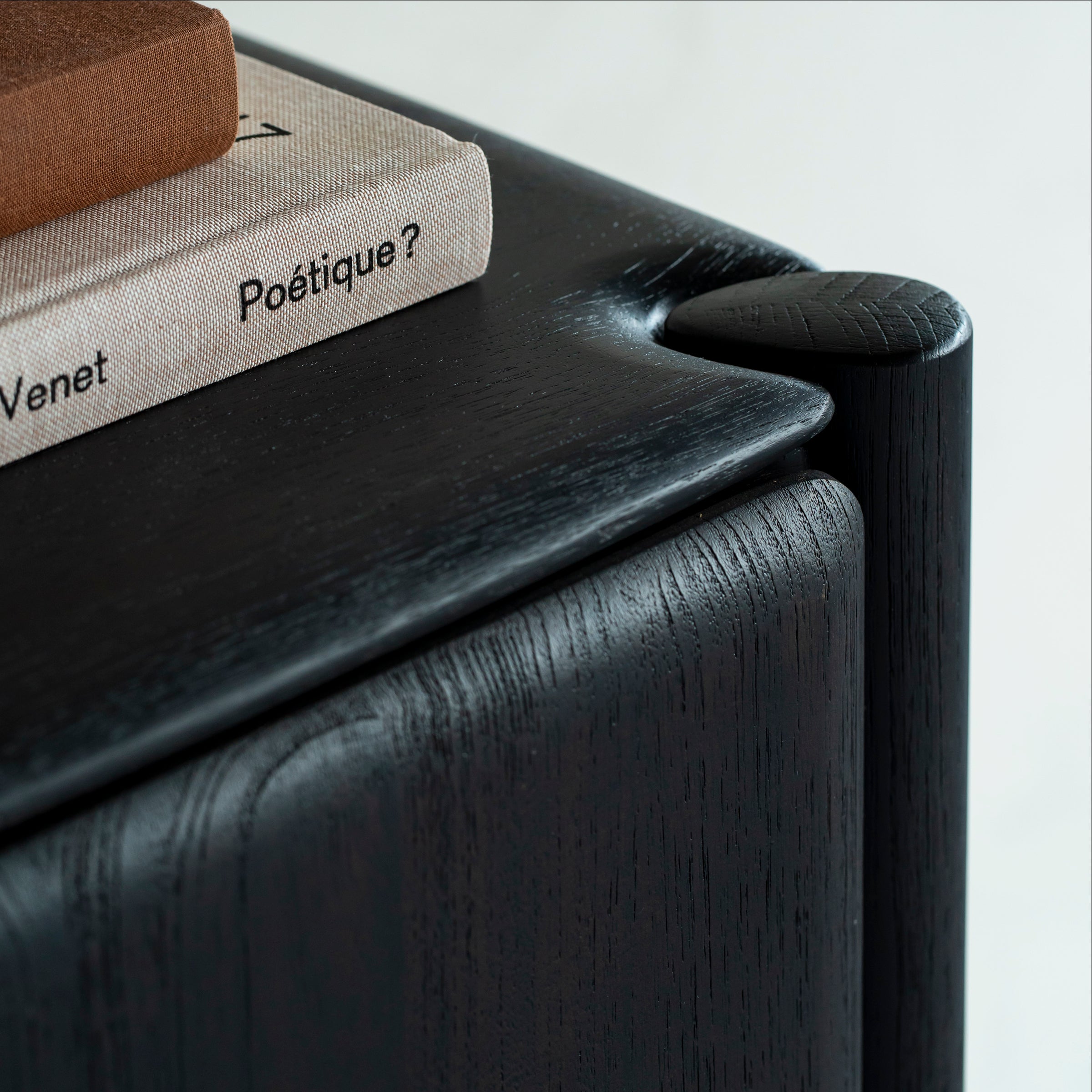 Close-up of the dark brown varnished oak corner detail on the Pi Sideboard with a book on top.