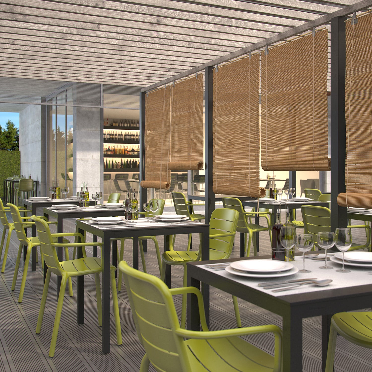 The outdoor restaurant seating area boasts rows of green chairs with powder-coated aluminum frames and Barcino Tables by Resol, set with white plates and glassware. Bamboo blinds hang from the pergola above, while shelves stocked with wine bottles are visible through the glass doors.