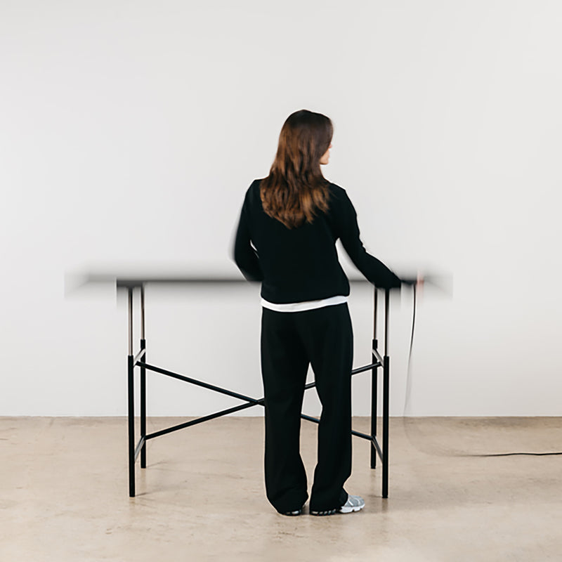 Person adjusting the height of the black steel frame Eiermann M Table in a minimalist room setting.