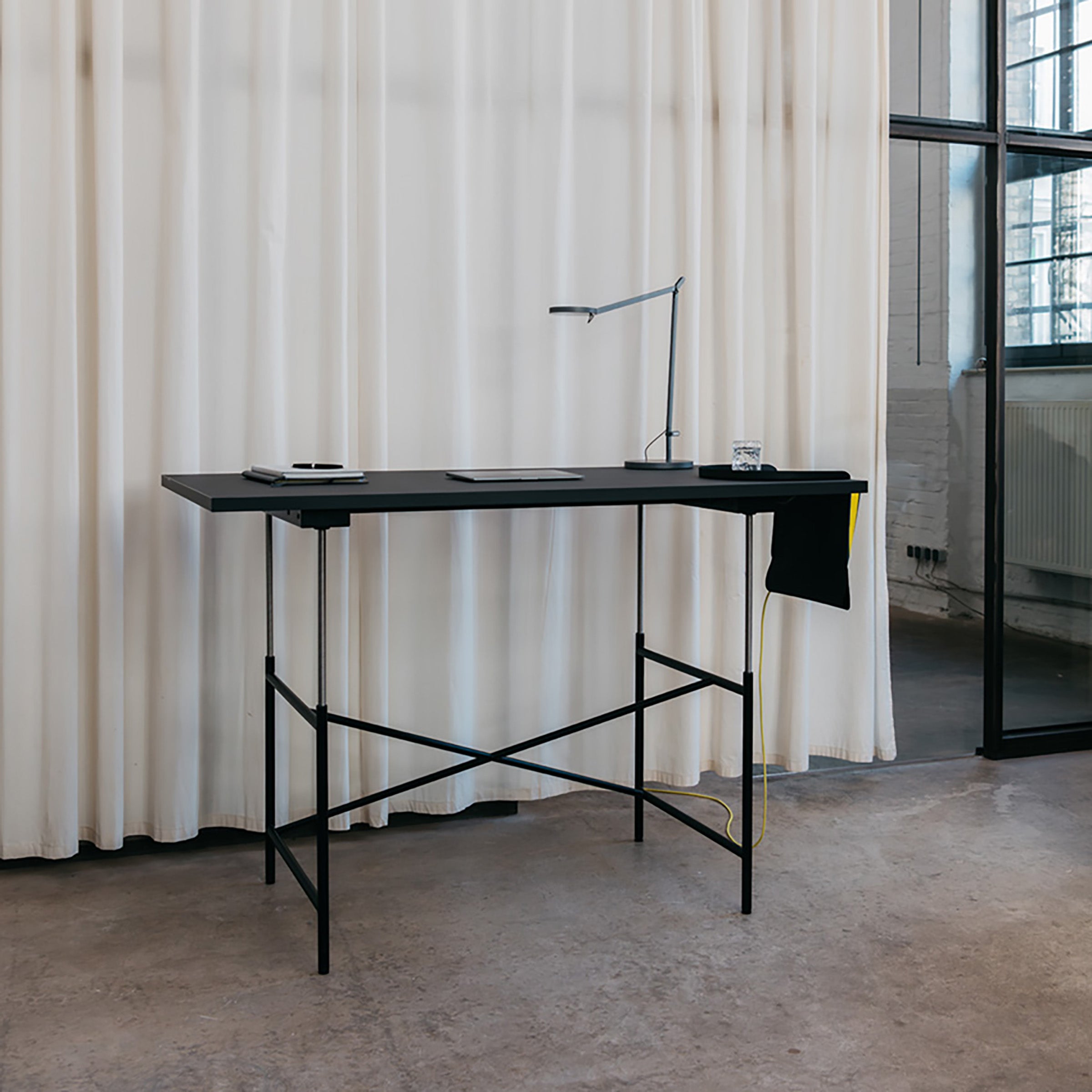 Eiermann M Table with black adjustable height frame and minimalist black tabletop in modern industrial room.