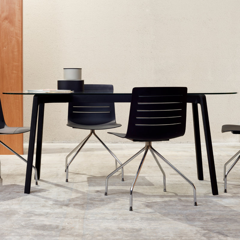 The modern dining area showcases the Resol Noren table, a sleek glass piece with a black frame, complemented by matching chairs with lacquered aluminum legs. This elegant setup embraces minimalism and sustainable production practices.