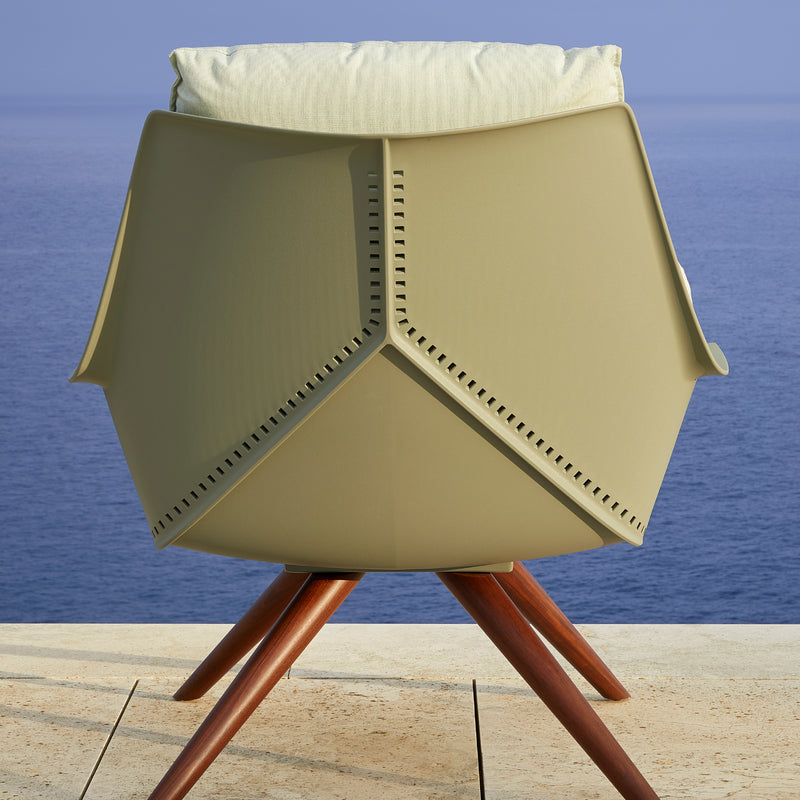 The Anou Wooden Legs armchair by Resol, featuring a beige cushion and wooden legs, graces the deck, perfect for indoor or outdoor use as it overlooks the serene blue sea.