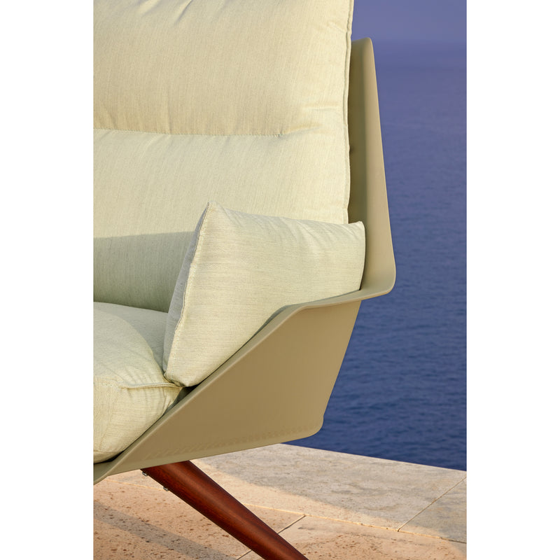 Close-up of a stylish Resol Anou Wooden Legs lounge chair with light green cushions on a beige stone surface, overlooking the calm blue ocean. Its sleek, minimalist design features angled wooden legs and is ideal for both indoor and outdoor use.