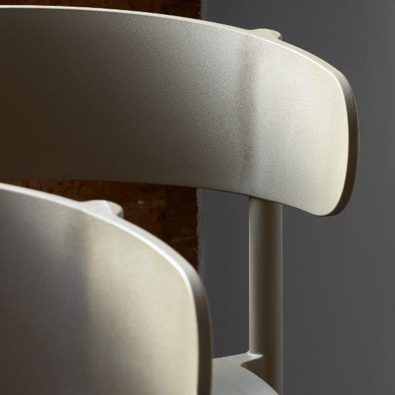 Close-up of the Resol Casino Chair, featuring a sleek, metallic finish and curved backrest. The lighting emphasizes its smooth texture and clean lines, set against a dark background, highlighting this modern sustainable furniture piece.