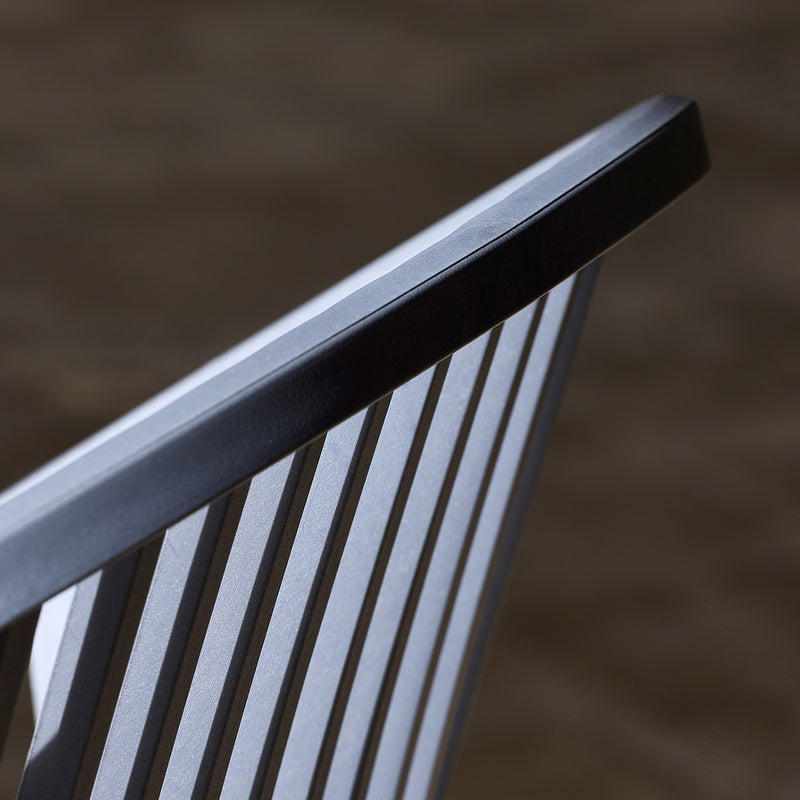 Close-up of the Bini Chair by Resol, showcasing its sleek black frame with vertical slats. The focus on the backrest highlights its modern design and smooth lines, crafted sustainably. A blurred background emphasizes the chairs elegant structure.