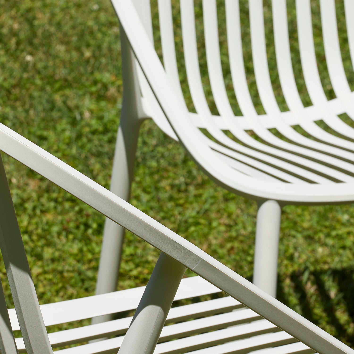 Close-up of two Bini Chairs by Resol on grass, showcasing intersecting lines and shadows. These innovative chairs feature a modern, minimalist design with curves and angles, crafted sustainably. The natural, vibrant green grass provides the perfect background.