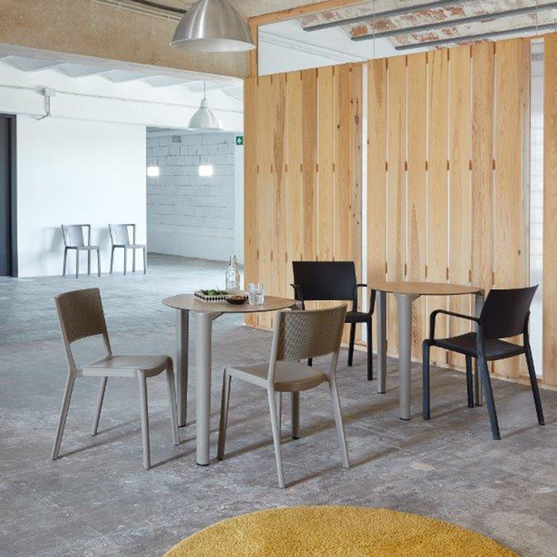 A modern, minimalistic room features two small round tables, each with stackable Fiona Armchairs by Resol in neutral tones. A wooden partition divides the space, and two more Fiona Armchairs are placed against a distant wall.