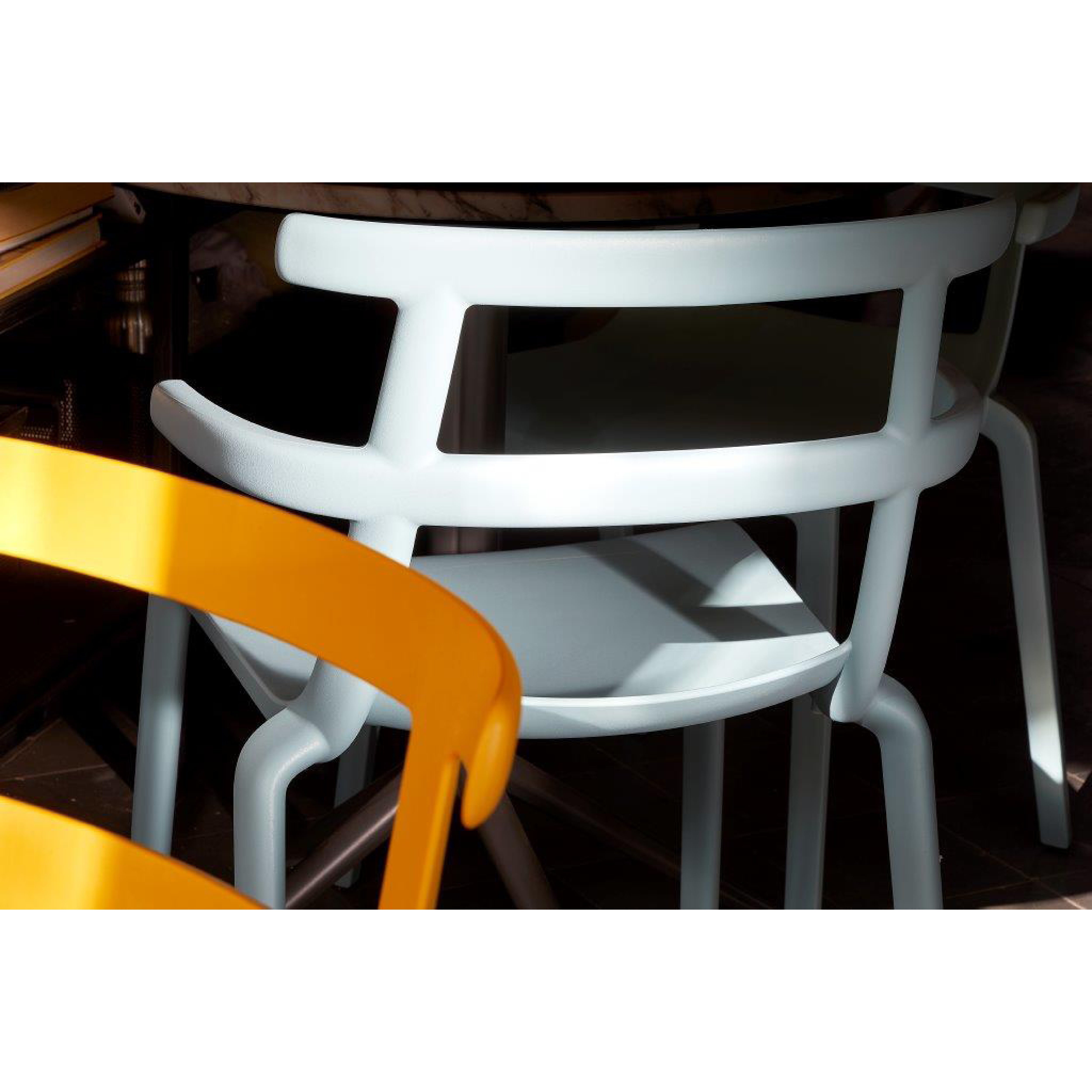 A close-up of two Tokyo Chairs by Resol features a yellow one with curved lines and a light blue minimalist design, both in sunlight. These chairs showcase shadows and are sustainably crafted for lasting quality.