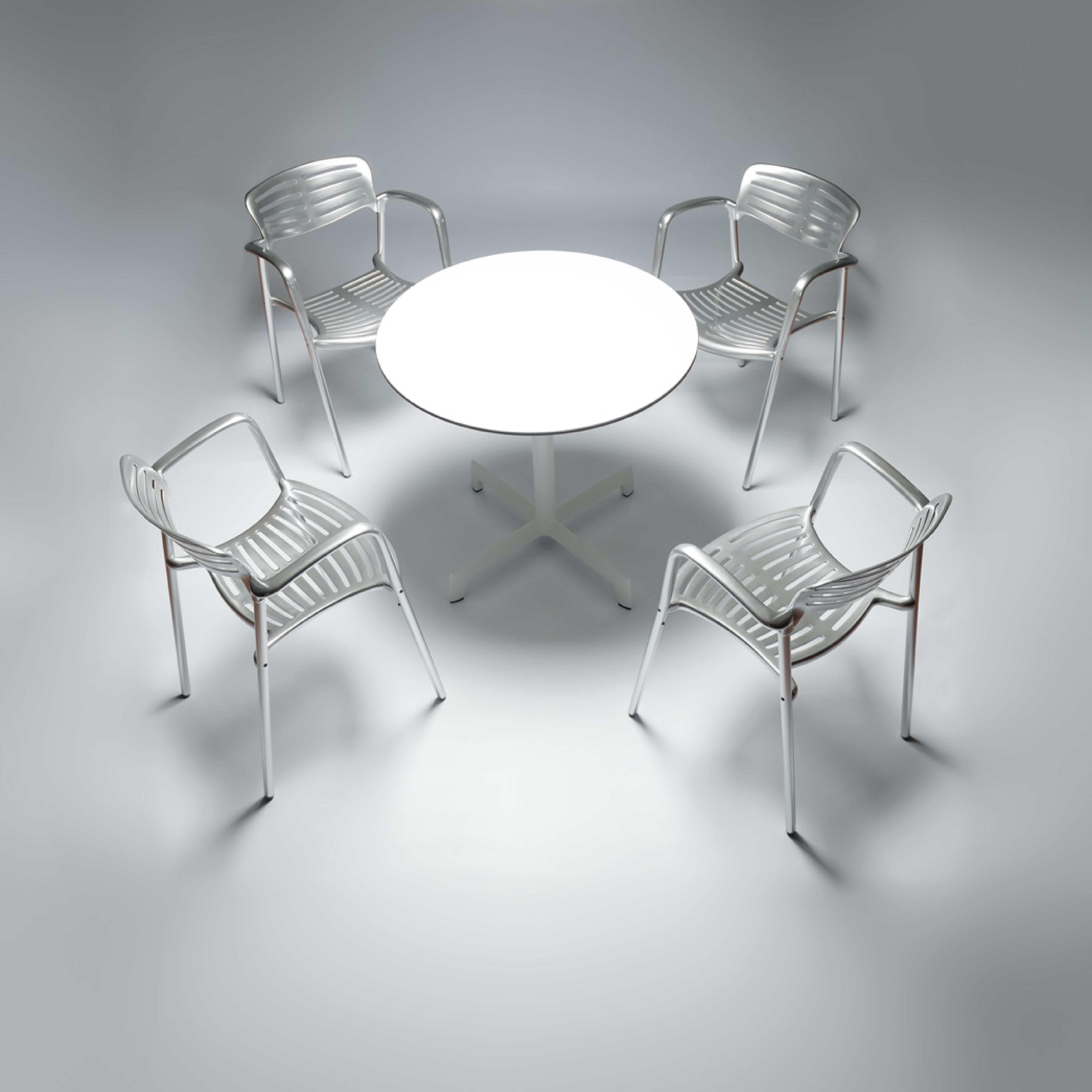 Four white Toledo Armchairs by Resol encircle a round white table in a minimalistic modern setting. Soft lighting highlights the clean design, crafted sustainably with UV protection for longevity.