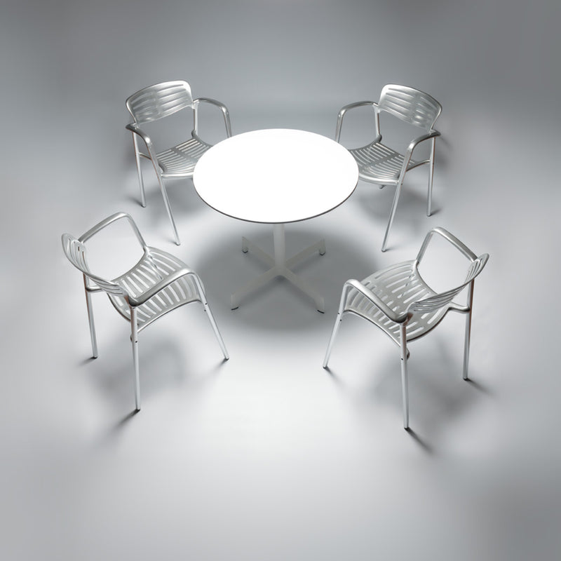 Four white Toledo Armchairs by Resol encircle a round white table in a minimalistic modern setting. Soft lighting highlights the clean design, crafted sustainably with UV protection for longevity.