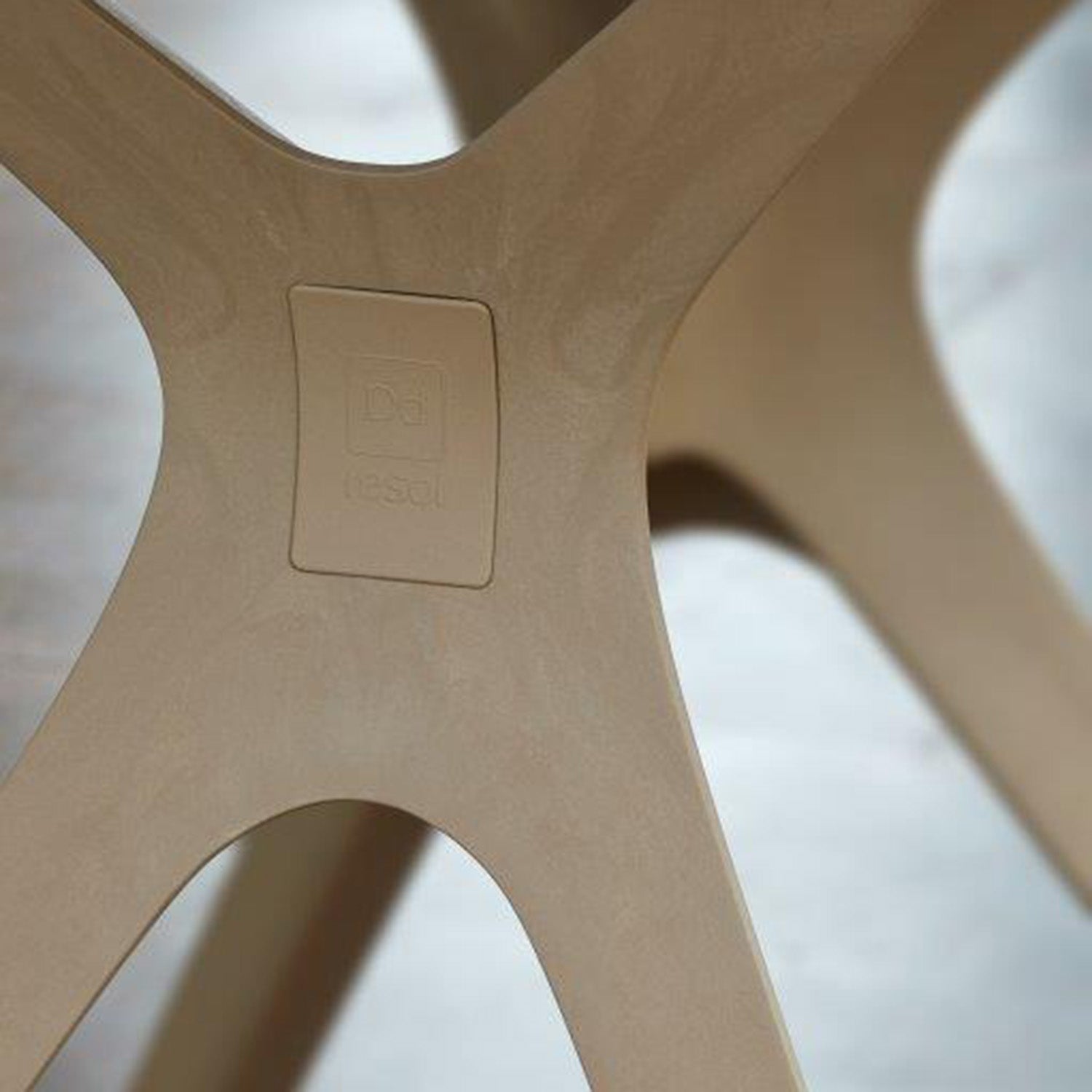 Close-up of the Vela Table S by Resol: a light brown plastic leg with a curved design and wood-like texture suitable for indoor/outdoor use. The recessed rectangular Resol logo is visible amid innovative furniture solutions against a blurred contrasting background.
