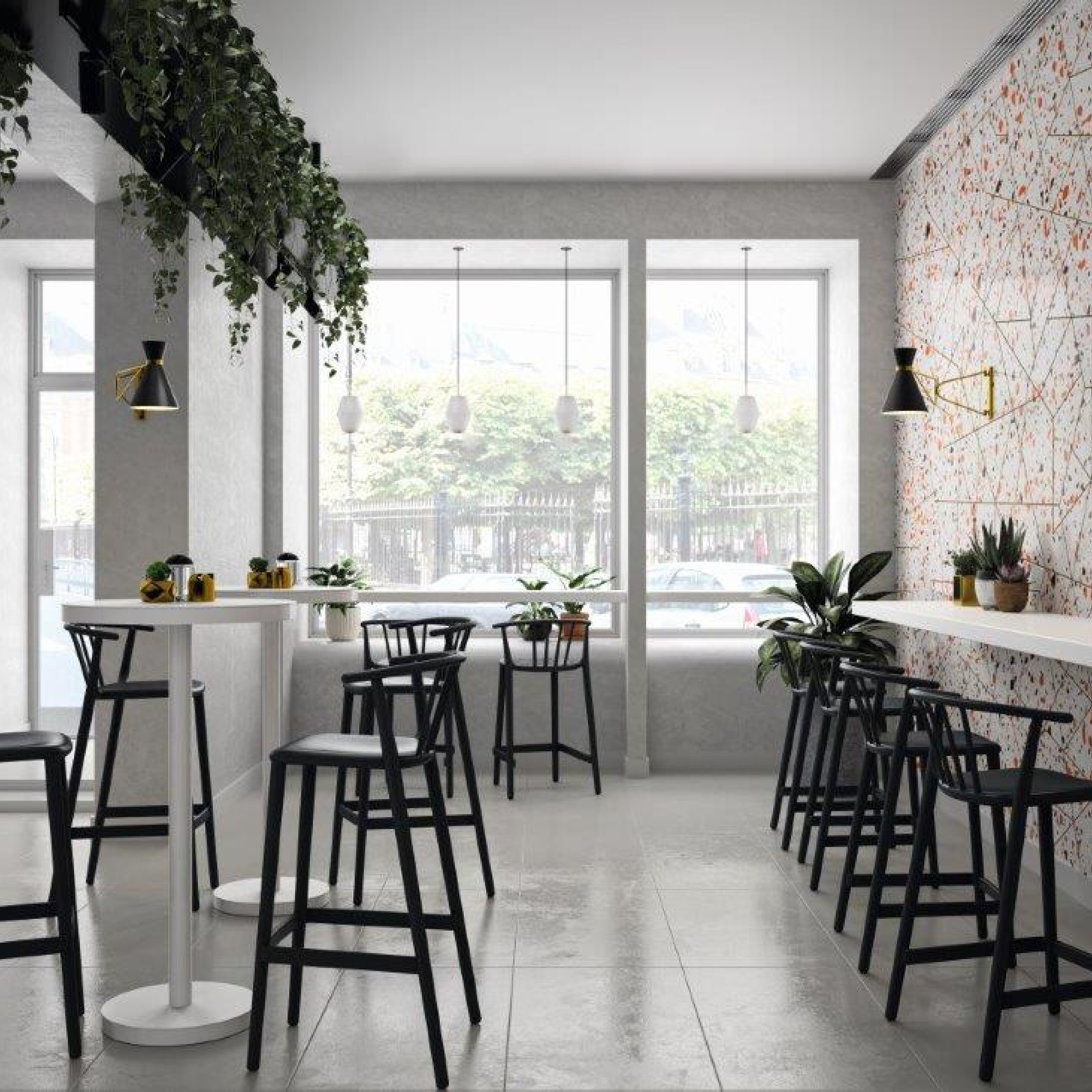A bright, modern cafe features high Woody Stools and tables from Resol, known for sustainable production. Hanging plants complement a geometric wall pattern. Large windows flood the minimalist decor with natural light and offer views of parked cars, enhancing the open, clean atmosphere.