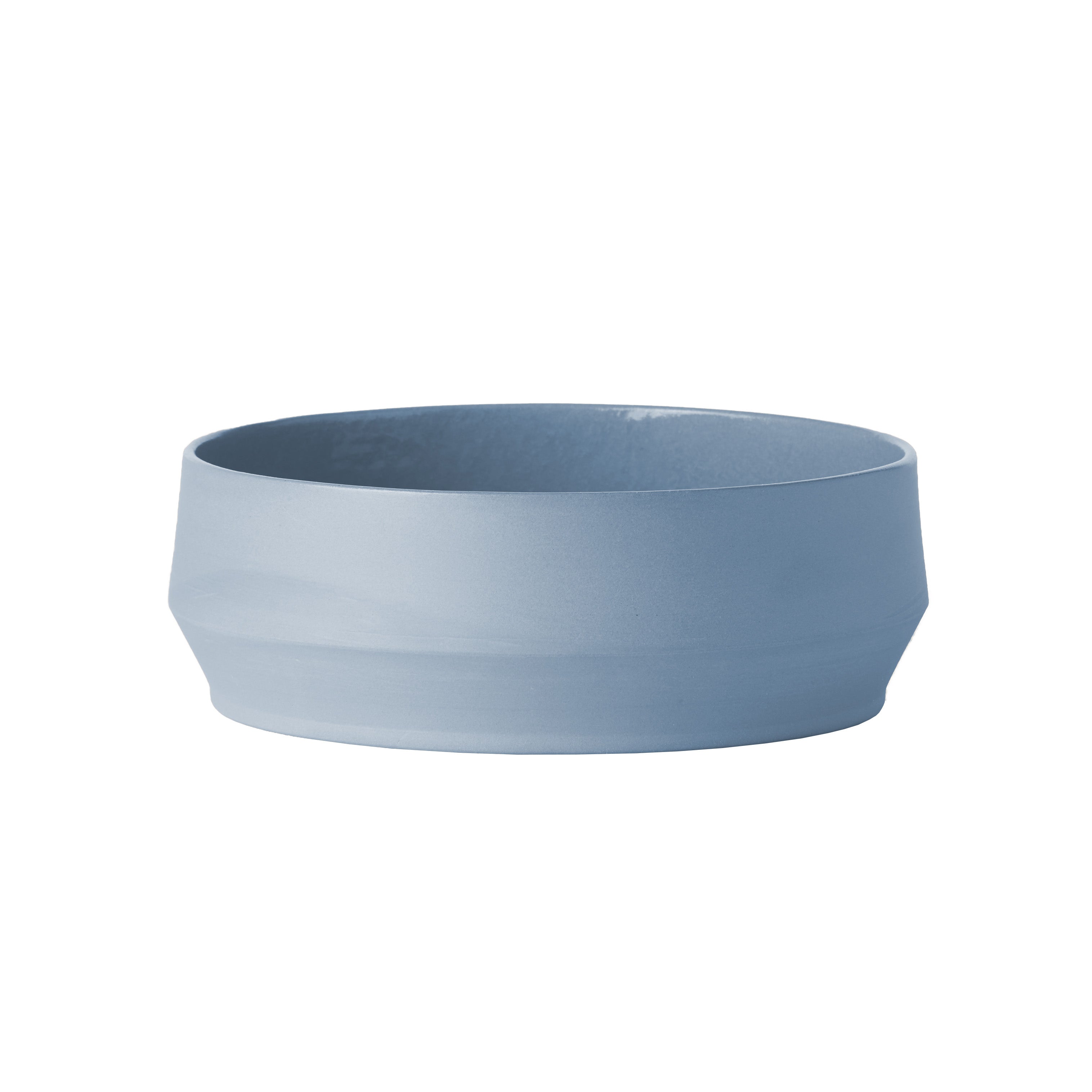 The Unison Soup Bowl - Sale by Schneid is a simple, light blue ceramic piece with a wide circular opening and subtle texture. It boasts a slightly tapered base and smooth matte finish for added elegance. Handmade in Germany, it is set against a plain white background.