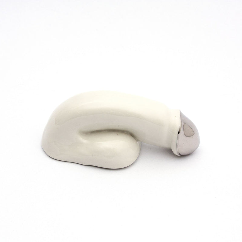 A handmade ceramic sculpture by Schwanzmanufaktur called A Decorative Sex - Chrome, features a stylized phallic shape on a white background, with a cream-colored body and distinctive metallic-tipped finish, highlighting its decorative allure.