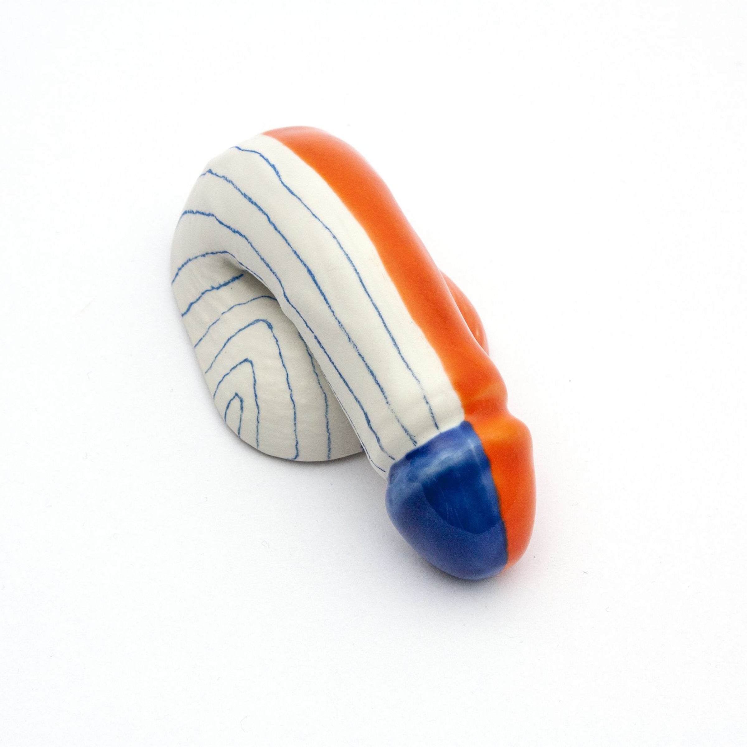 A Decorative Sex - Go Mets is a small abstract ceramic sculpture by Schwanzmanufaktur, crafted in Austria. It features a coiled form with horizontal navy stripes on white porcelain, accented by bold orange and a blue tip.
