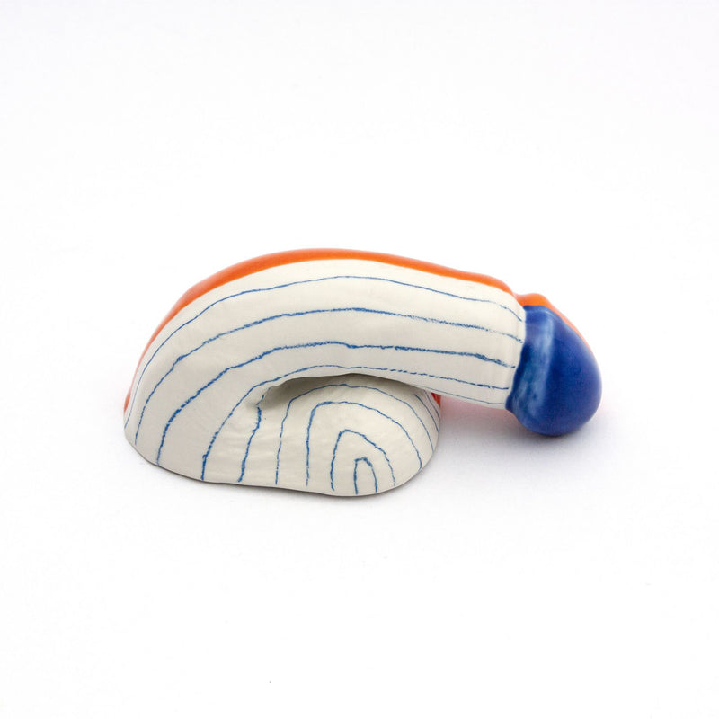 This abstract ceramic sculpture, A Decorative Sex - Go Mets, is handmade in Austria by Schwanzmanufaktur. It features a coiled form with alternating blue and white stripes, a solid blue end, and a rounded orange stripe accenting the top edge on a plain white backdrop.