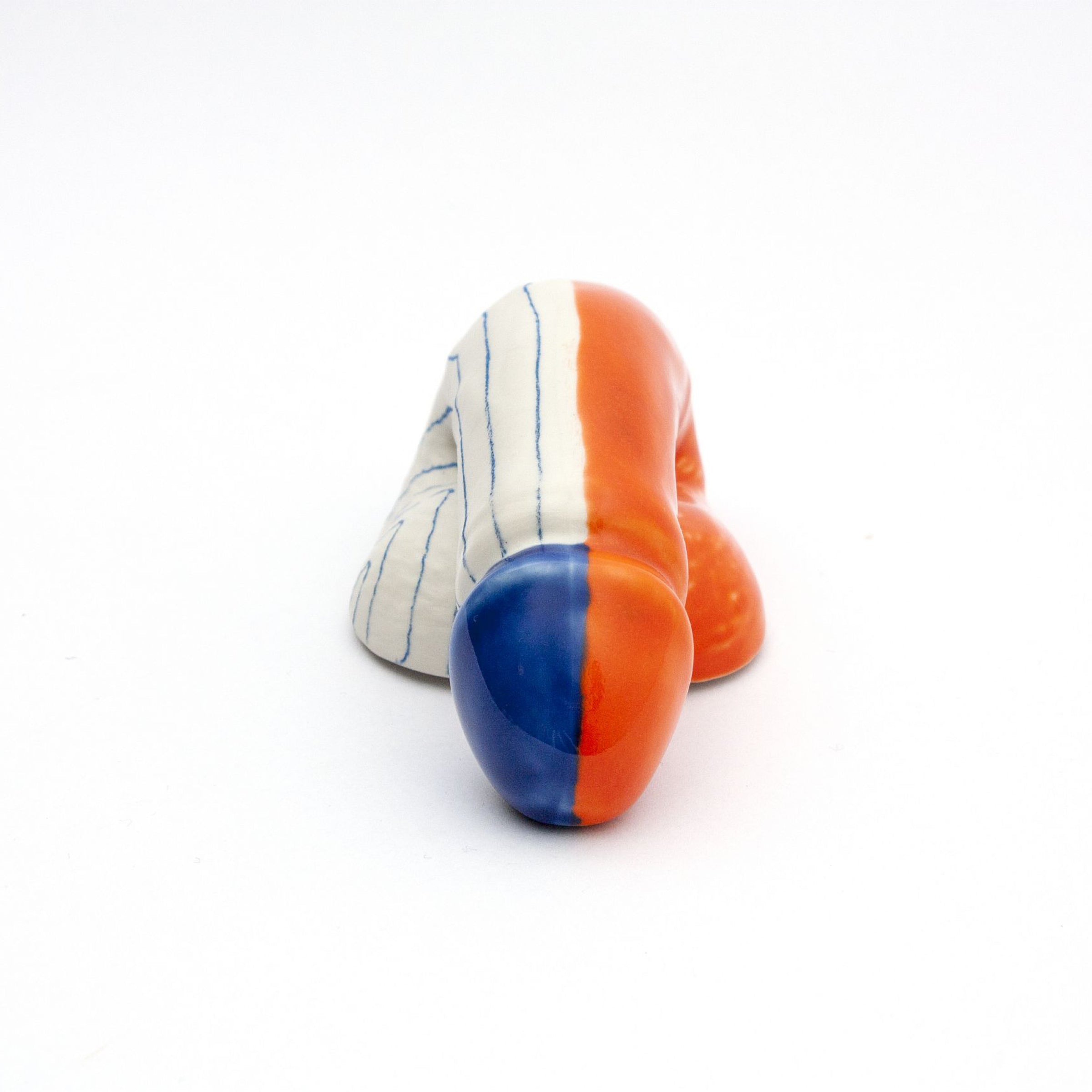 The A Decorative Sex - Go Mets by Schwanzmanufaktur is a handmade Austrian porcelain sculpture featuring a crouching figure with an orange and blue head, seamless color blending on the body against a white backdrop, and vertical stripes in orange, blue, and white.