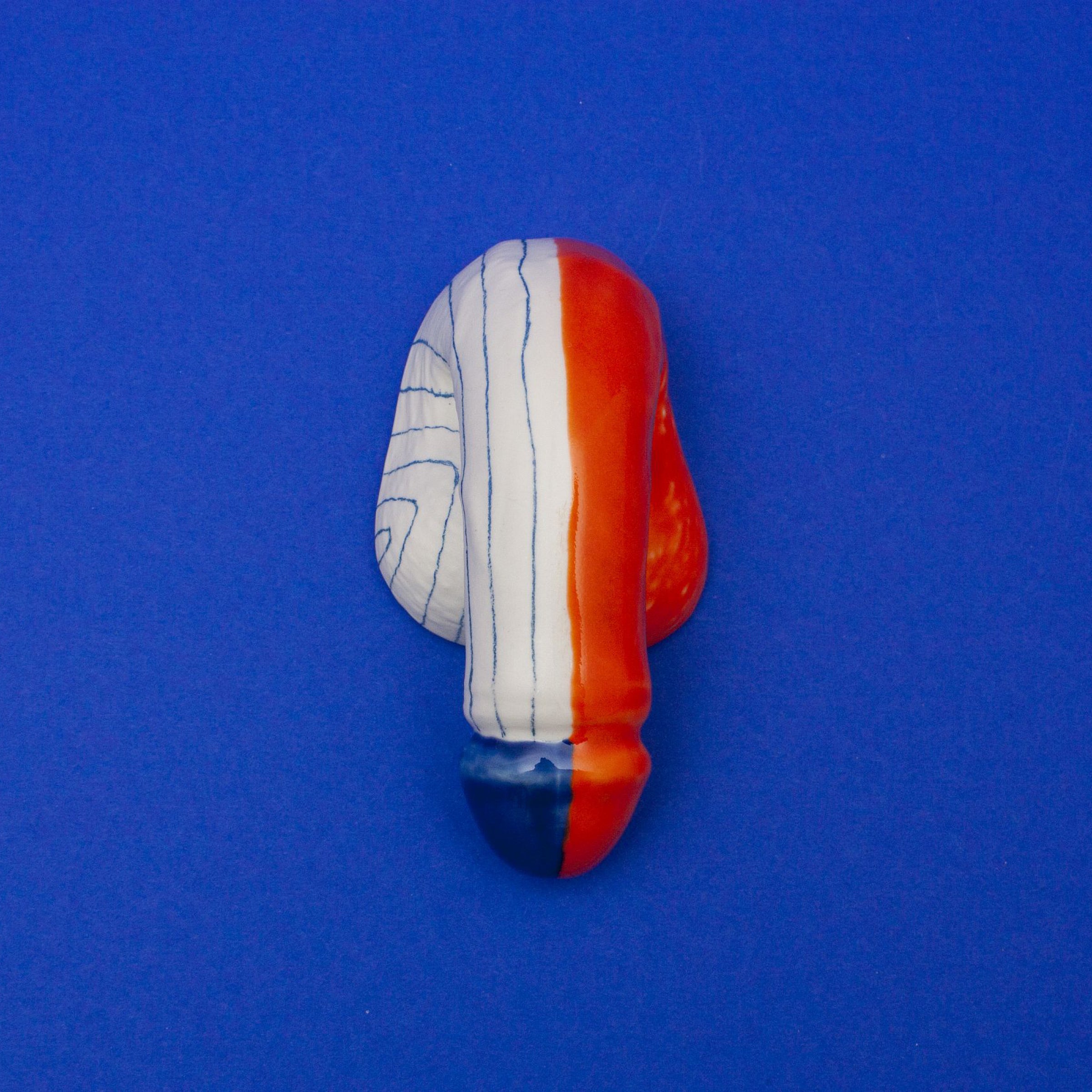 The porcelain object, named A Decorative Sex - Go Mets by Schwanzmanufaktur, is handmade in Austria. It resembles a nose and showcases an abstract design in blue, white, and red with wavy lines on the white section against a solid blue background.