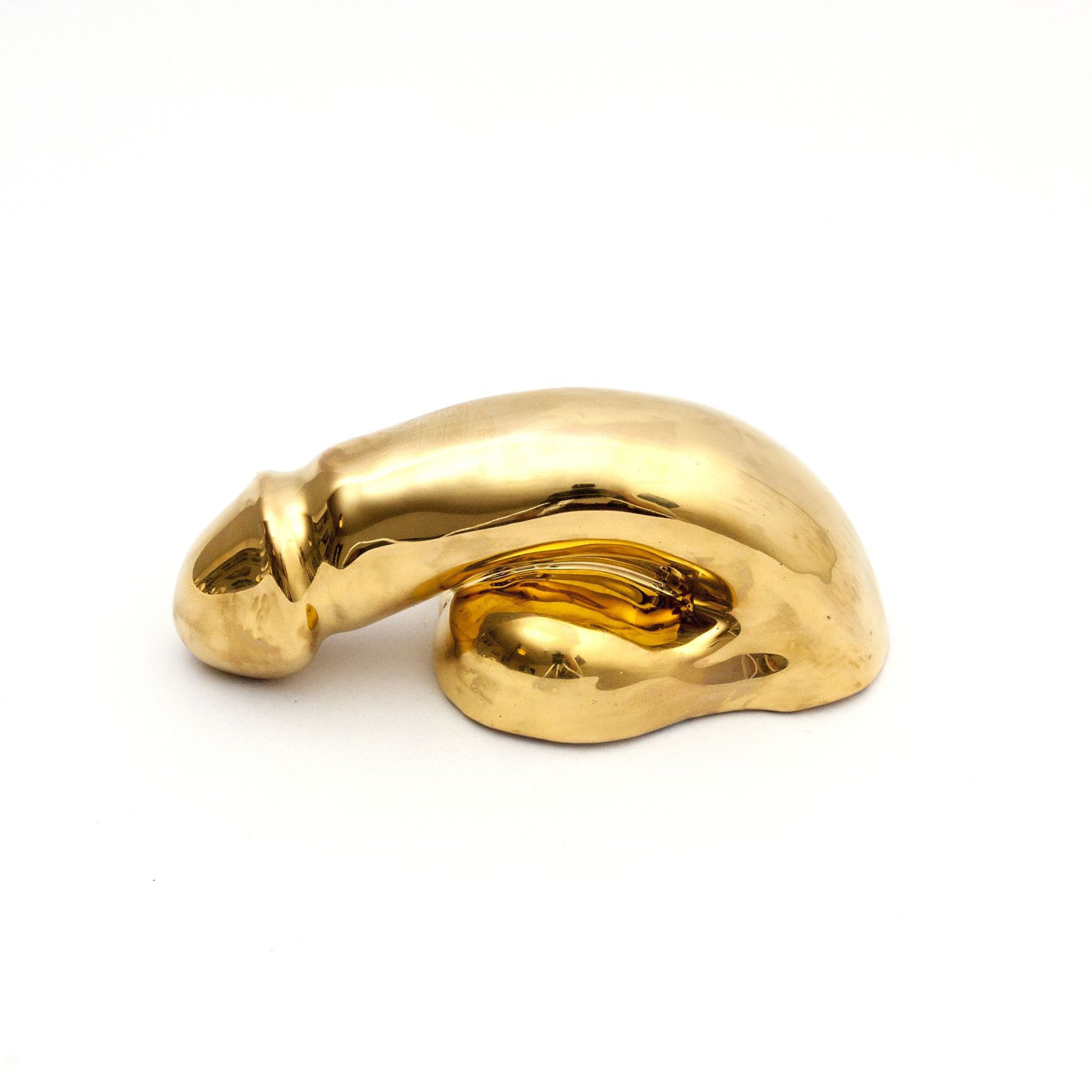A Decorative Sex - Gold sculpture by Schwanzmanufaktur rests against a white backdrop. Its glossy, reflective surface and organic, curved shape showcase the elegance reminiscent of handmade porcelain in a modern, abstract style.