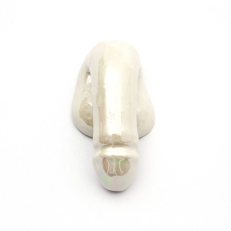 A Decorative Sex - Pearl by Schwanzmanufaktur is a ceramic sculpture resembling an abstract human nose on a white background, exemplifying Austrian craftsmanship. The wall art features a glossy finish with subtle color variations for a smooth, polished look.